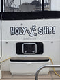Holy Ship boat name in white outlined lettering with an anchor, on a cream transom