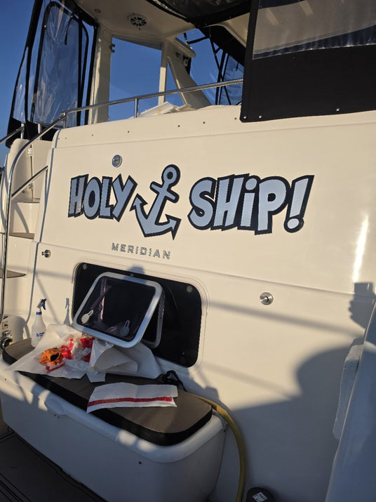 Holy Ship lettering on the transom during installation, with application paper on the bench